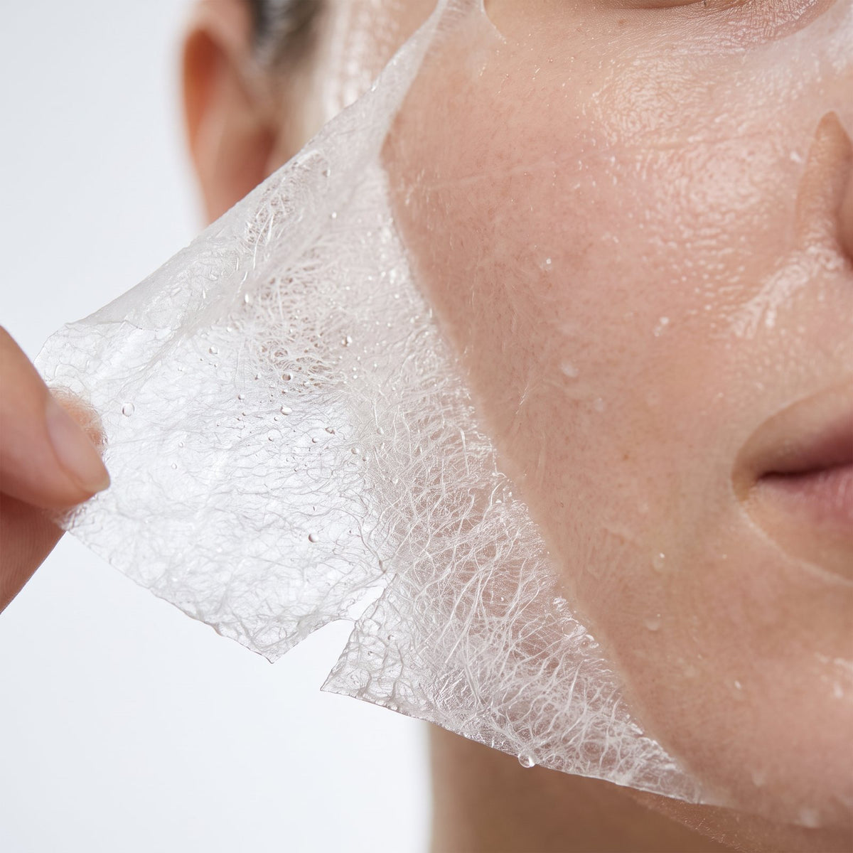 Close-up of a translucent bio-cellulose sheet being peeled from the cheek